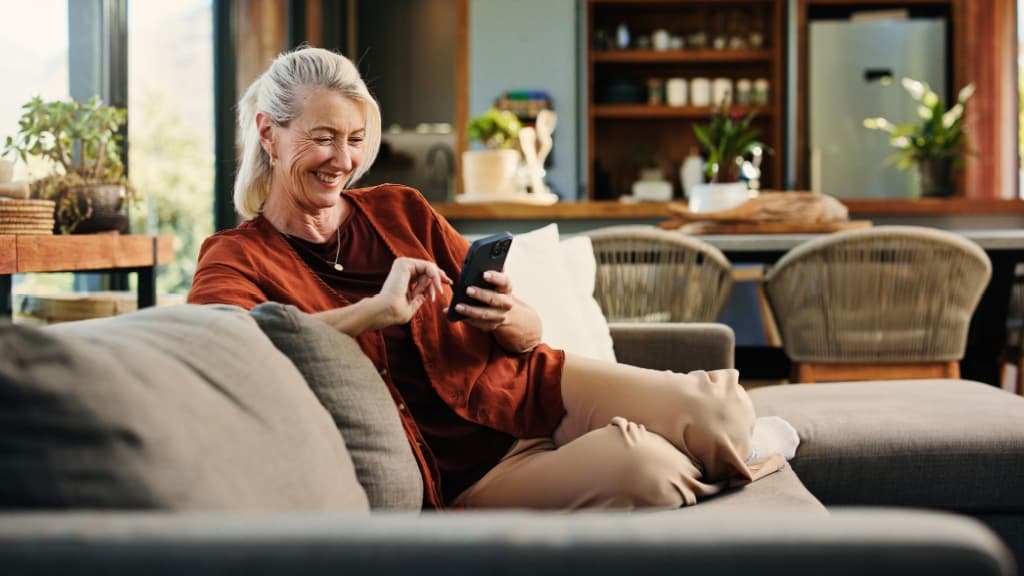 Mature woman, phone and laugh on sofa with texting, notification and funny chat in living room at house.