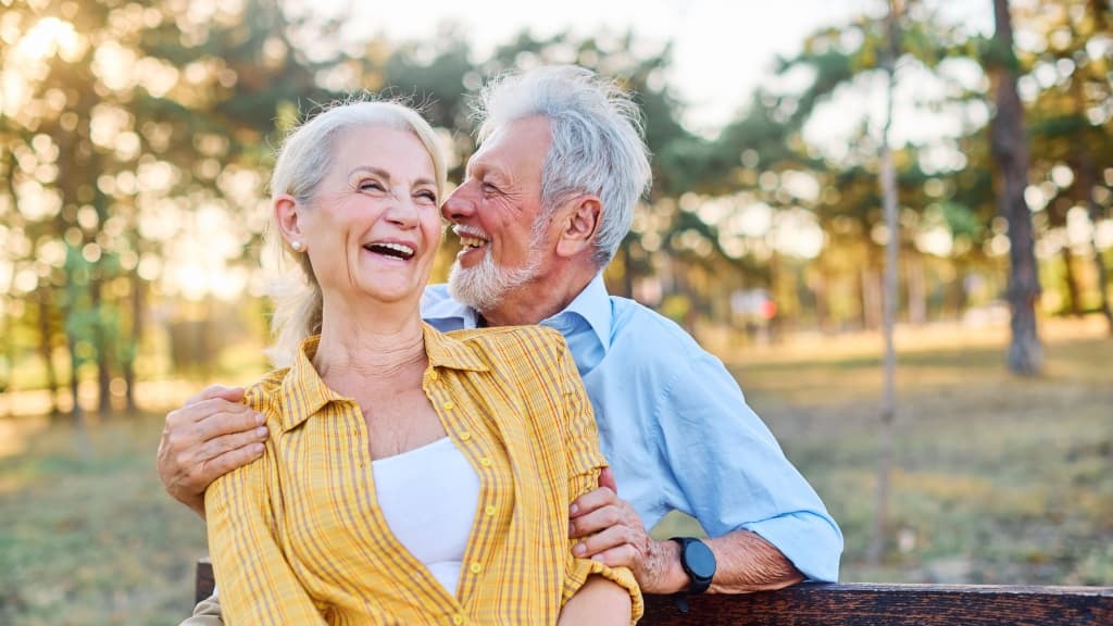 Happy active senior couple having fun talking and hugging sitting on a bench.