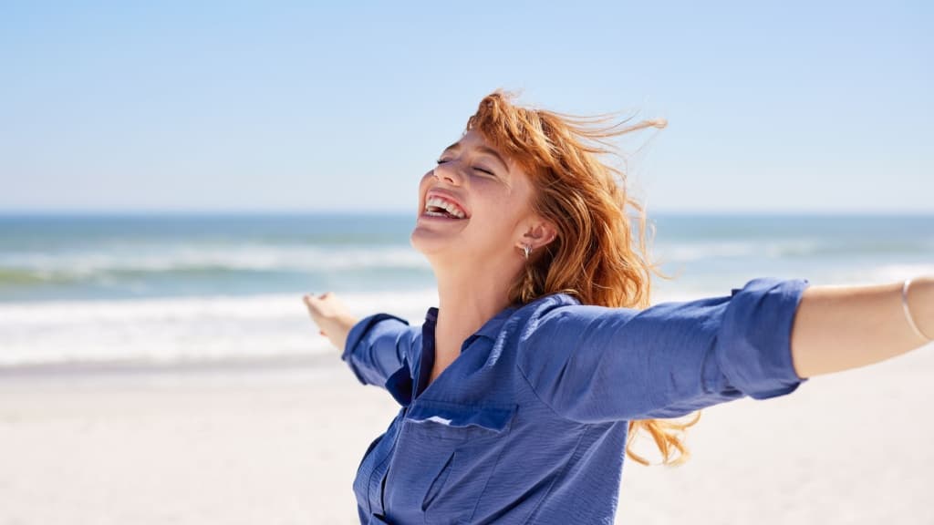 Beautiful girl in casual outfit enjoying sunbath at beach with arms outstretched.