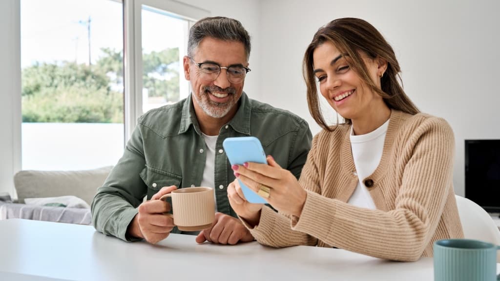 Smiling mature older man and woman holding cellphone browsing internet