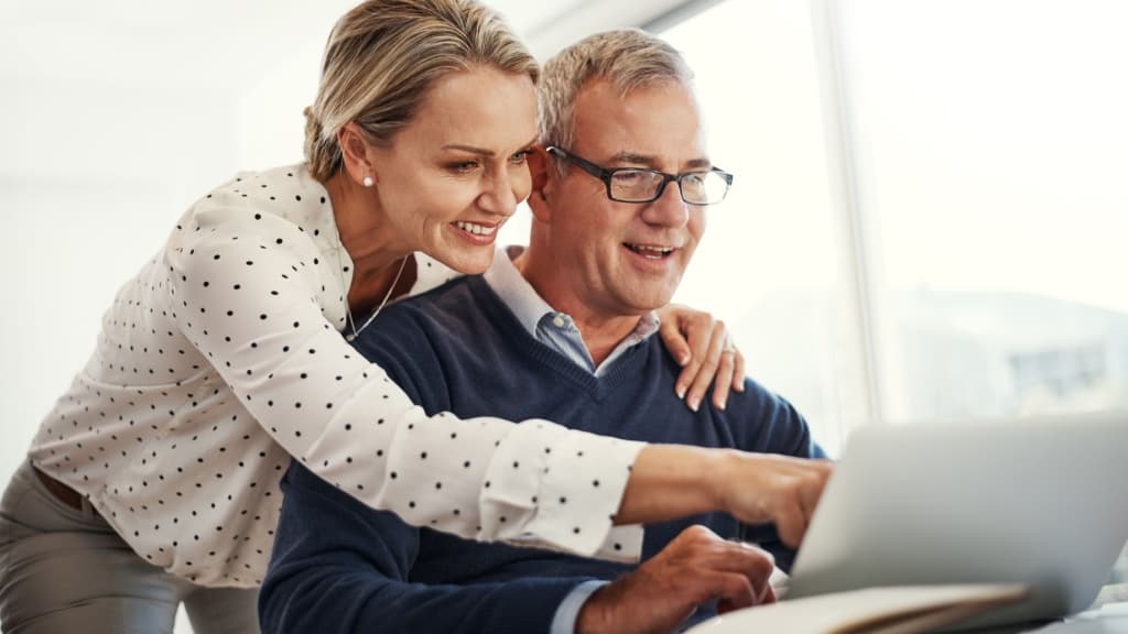 Hugging mature couple pointing at laptop.